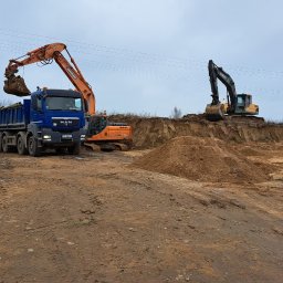 FIRMA USŁUGOWO-TRANSPORTOWA GRE-CAR ŁATA GRZEGORZ - Żółty walec, niebieska ciężarówka MAN i pomarańczowa koparka Doosan w trakcie prac ziemnych. W tle koparka Volvo na skarpie. Prace ziemne w toku.