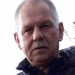 Portret starszego mężczyzny z wąsami, ubranego w czarną kurtkę, na rozmytym tle.