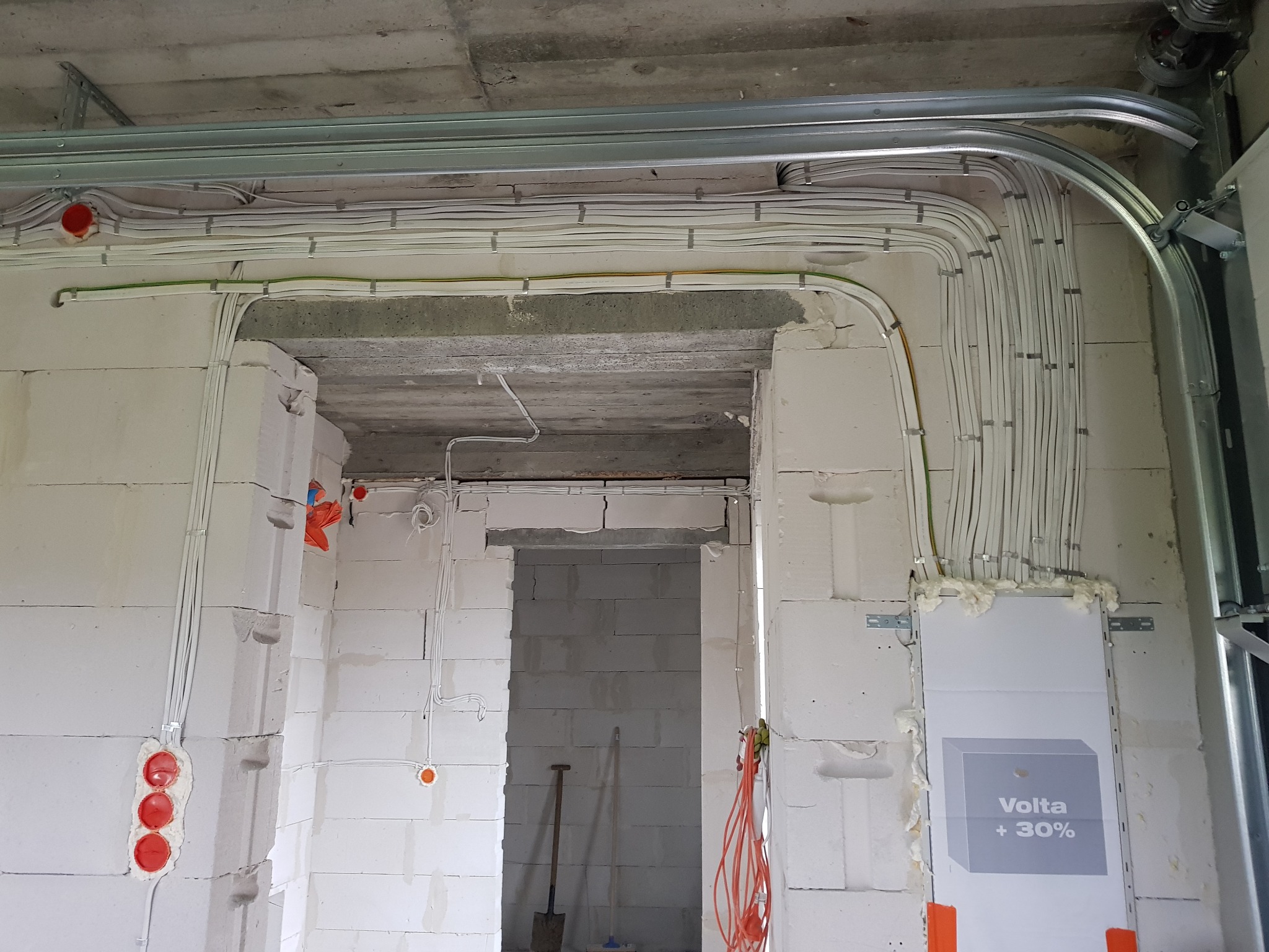 Nowe okablowanie elektryczne w surowym wnętrzu, przewody zabezpieczone klamrami, widoczne puszki instalacyjne w ścianie z betonu komórkowego, szyna montażowa pod sufitem, tablica rozdzielcza Volta...