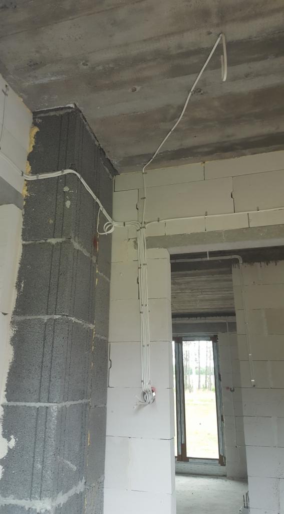 Surowe wnętrze w trakcie budowy z widocznymi przewodami elektrycznymi zamocowanymi do ścian z betonu komórkowego i sufitu, z puszkami instalacyjnymi bez osprzętu.
