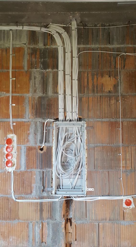 Rozprowadzenie przewodów elektrycznych w ścianie z cegły, widoczne puszki instalacyjne i kable w peszlach.