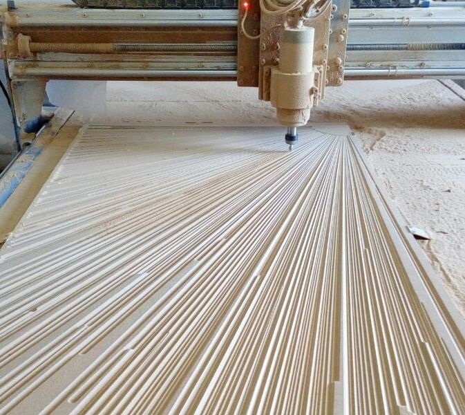 Frezarka CNC wycina wzór promieni na płycie drewnianej, widoczne wióry i pył drzewny.