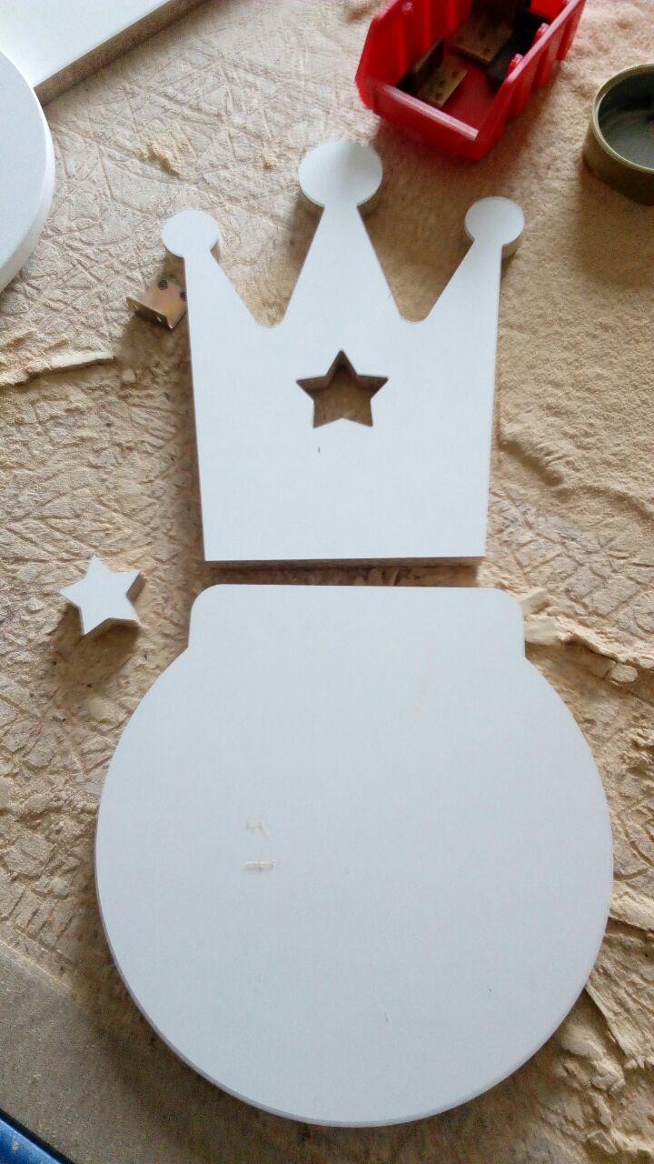 Niedokończona drewniana korona z wyciętą gwiazdą i okrągła podstawa obok małej drewnianej gwiazdki na tle warsztatu.