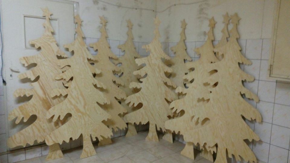 Rząd wyciętych z jasnej sklejki, surowych choinek z gwiazdą na czubku, opartych o ścianę wyłożoną kafelkami.