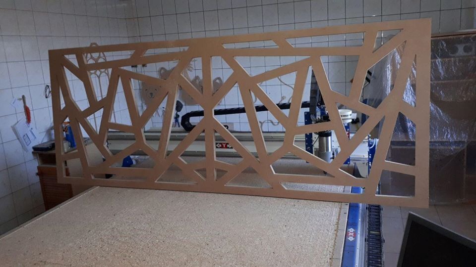 Ażurowy panel dekoracyjny z MDF o geometrycznym wzorze, wycięty na frezarce CNC, w warsztacie z kafelkowymi ścianami.