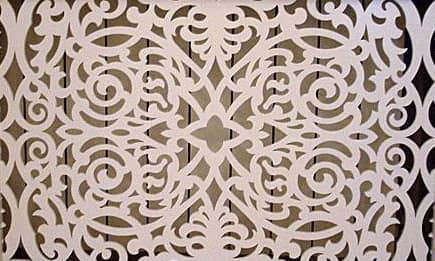 Dekoracyjna, ażurowa płyta z białego tworzywa z symetrycznym, florystycznym wzorem na tle drewnianych desek.