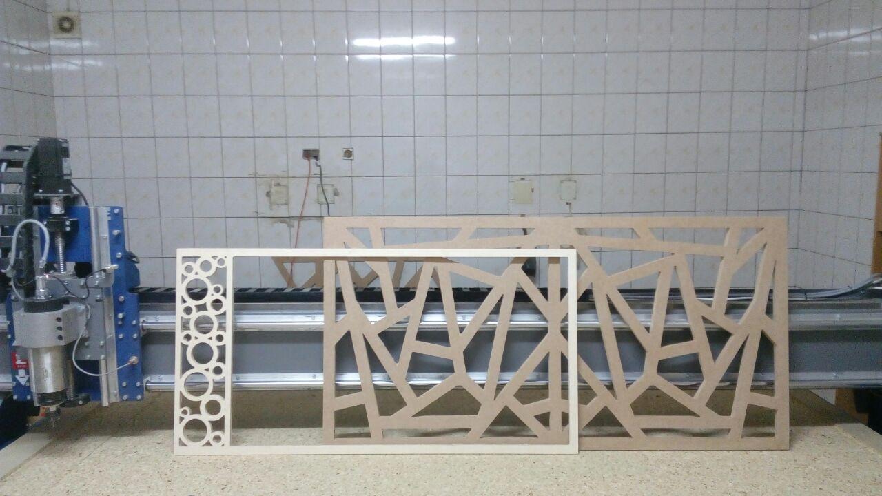 Panel dekoracyjny z MDF z wyciętymi wzorami geometrycznymi i okrągłymi otworami, wykonany przy użyciu frezarki CNC, widocznej w tle.