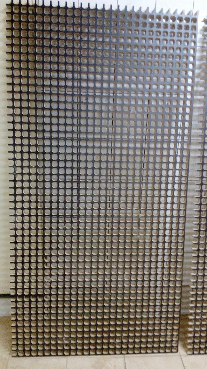 Metalowa siatka z regularnymi kwadratowymi otworami, widoczne ślady obróbki na krawędziach, surowe tło.