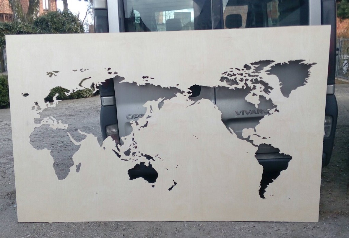 Drewniana płyta z wyciętym laserowo motywem mapy świata, oparta o tylną klapę samochodu dostawczego.