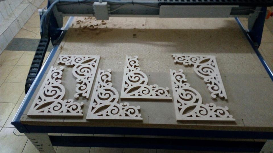 Wycinane laserowo drewniane elementy dekoracyjne z ażurowym wzorem, leżące na stole frezarki CNC po obróbce.