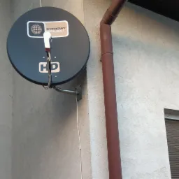 Antena satelitarna Cyfrowy Polsat HD zamontowana na elewacji budynku obok rury spustowej, widok z dołu.