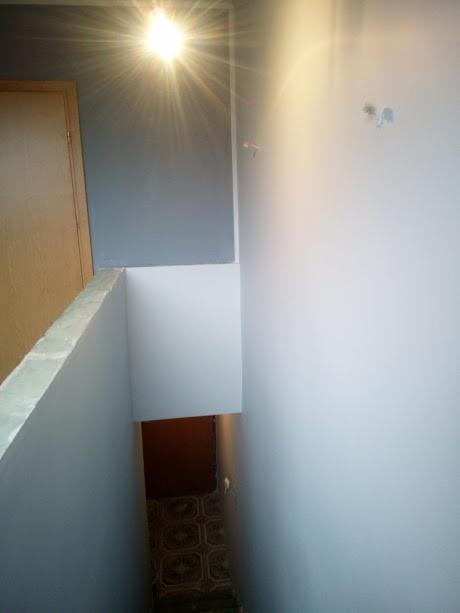 Świeżo pomalowane ściany w jasnych odcieniach szarości i bieli, widoczne ślady po instalacji elektrycznej, fragment korytarza z wzorzystą podłogą w tle.