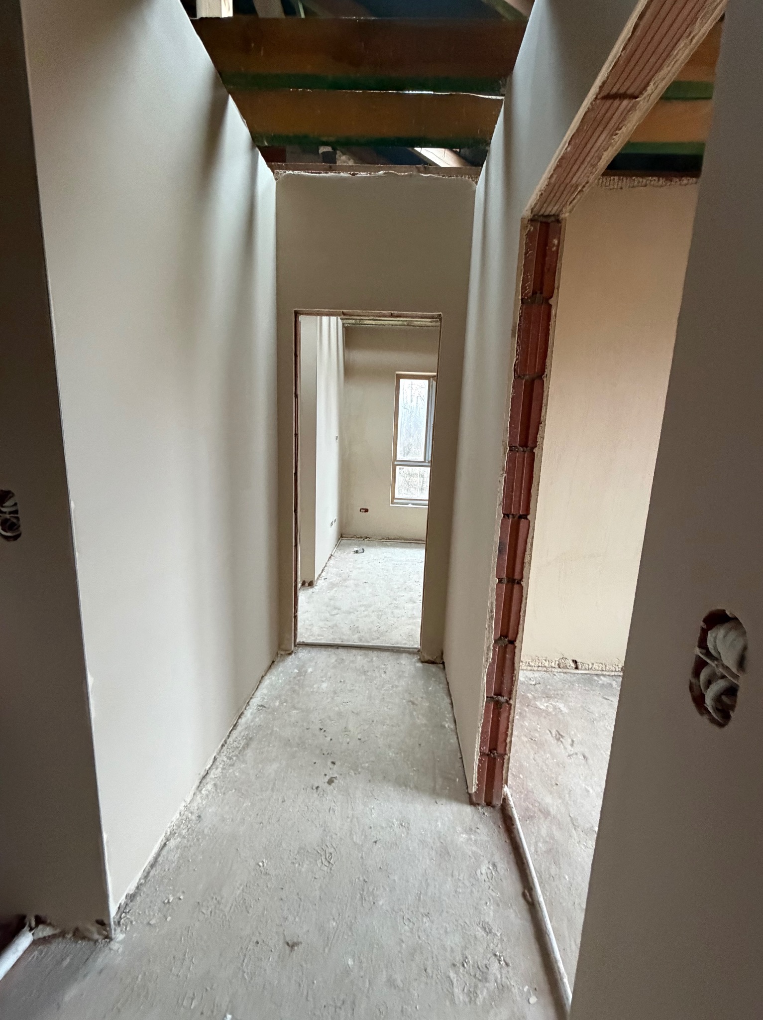 Wnętrze po nałożeniu gładzi gipsowej w Łodzi. Widoczne ściany i sufit po tynkowaniu, przygotowane do dalszych prac wykończeniowych. Surowy stan podłogi.