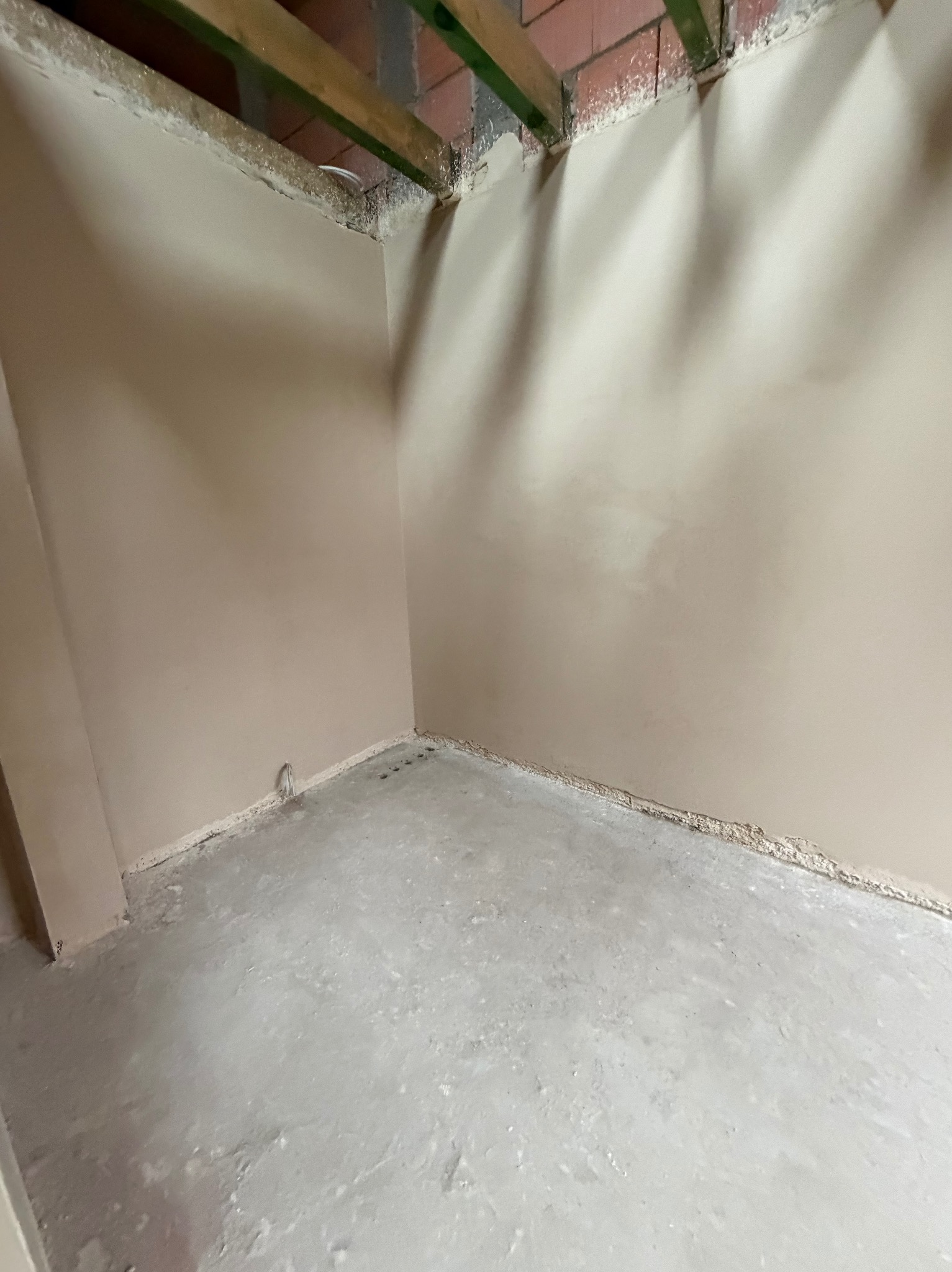 Wnętrze po nałożeniu gładzi gipsowej na ścianach i wylewce na podłodze. Widoczne drewniane elementy konstrukcyjne pod sufitem i wystający przewód elektryczny.