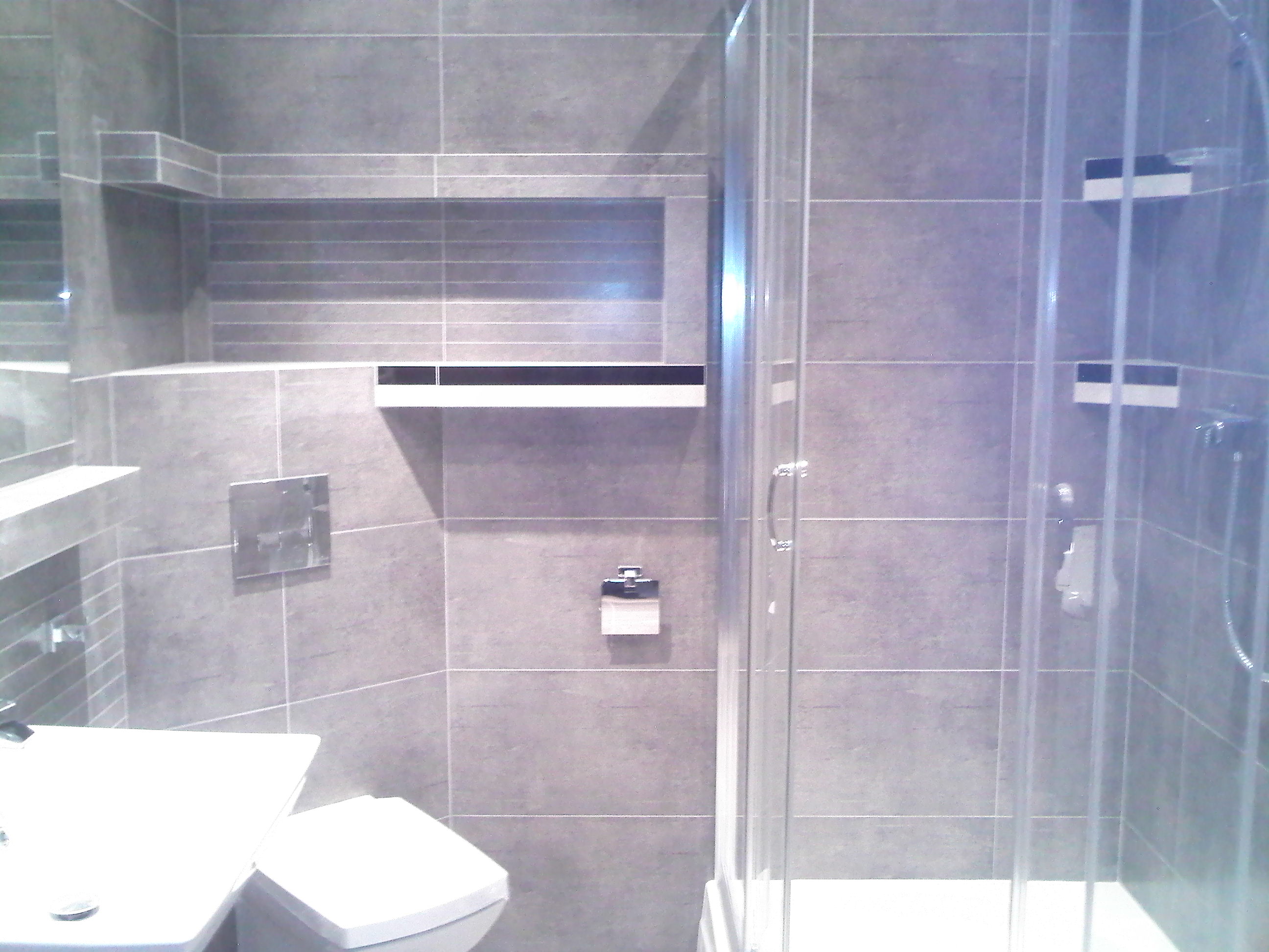 Nowoczesna łazienka z szarymi płytkami, kabiną prysznicową i wnęką z półkami wykończonymi czarnymi akcentami.