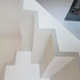 Wnętrze klatki schodowej z widocznymi schodami po remoncie, świeżo pomalowane na biało, z otwartą puszką instalacyjną na suficie.