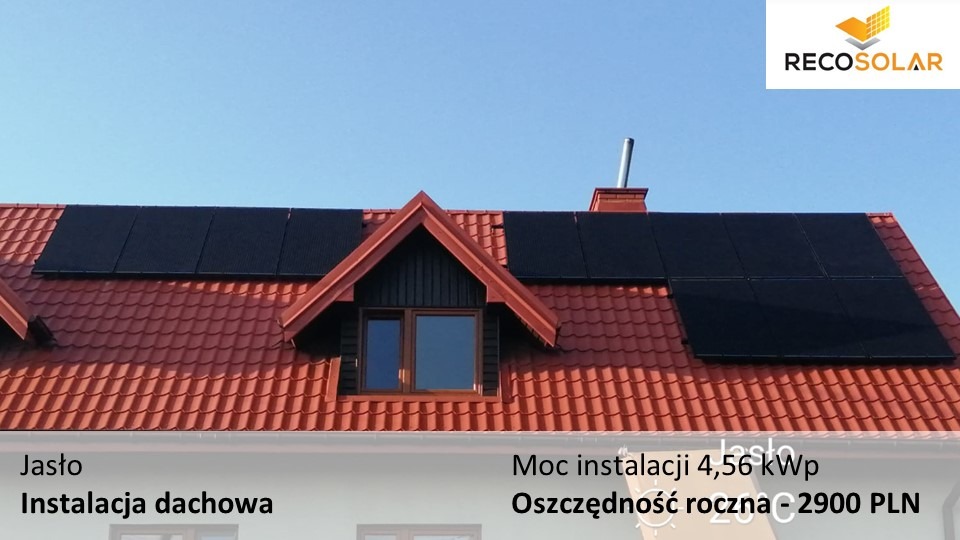 Instalacja paneli słonecznych Full Black na dachu domu z czerwoną dachówką, widoczny komin i okno na poddaszu, logo firmy RECO Solar w prawym górnym rogu.