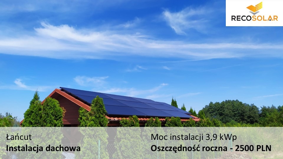 Instalacja paneli słonecznych na dachu domu jednorodzinnego w Łańcucie, widok z poziomu gruntu w słoneczny dzień, niebieskie niebo z lekkimi chmurami, logo firmy RecoSolar w prawym górnym rogu.