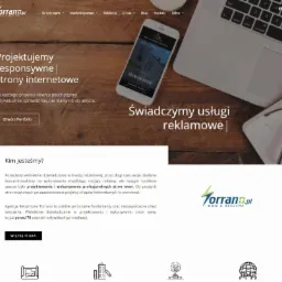 Ekran laptopa z wyświetloną stroną internetową torrano.pl, obok smartfon z prezentacją strony Premium House, notatnik z okularami i klawiatura, całość na drewnianym biurku.