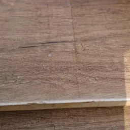 Stos brązowych blatów z widoczną strukturą drewna i niewielkimi uszkodzeniami powierzchni, oświetlonych naturalnym światłem.