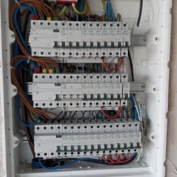 Otwarta skrzynka elektryczna z widocznymi bezpiecznikami, przewodami w różnych kolorach i odgromnikami Dehn, zamontowana na surowej ścianie przed wykończeniem.