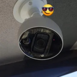 Kamera monitoringu kopułkowa zamontowana na suficie, widok z dołu, z widocznym fragmentem nieba w tle.