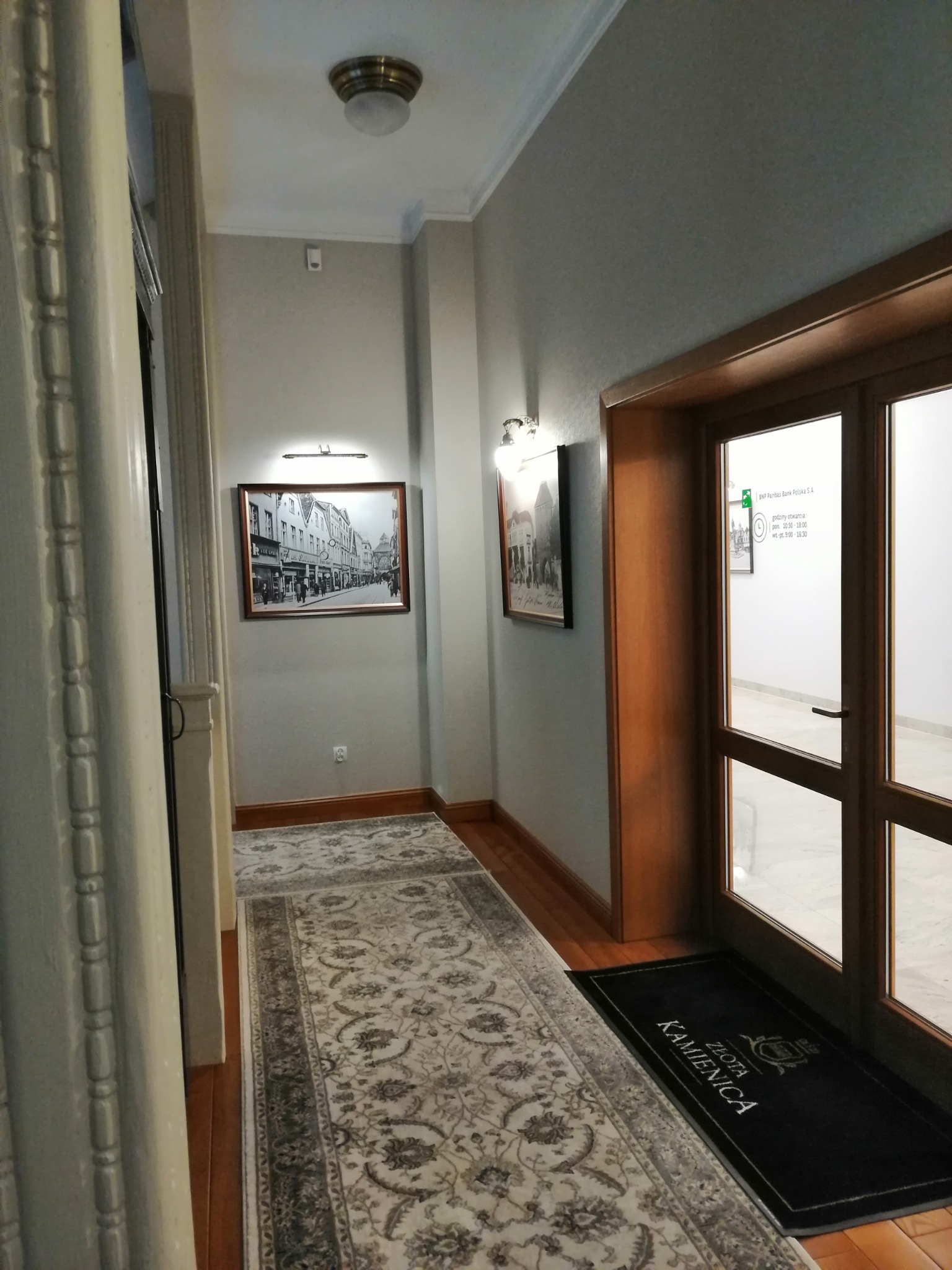 Korytarz z dywanem w budynku Złota Kamienica, z czarno-białymi zdjęciami na ścianach i drewnianymi drzwiami z widocznym logo BNP Paribas Bank Polska S.A.