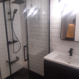 BAS Usługi Remontowo-Budowlane - Nowoczesna łazienka z kabiną prysznicową typu walk-in z czarnymi elementami, białe płytki typu metro na ścianach, czarna szafka pod umywalką i wzorzysta podłoga.