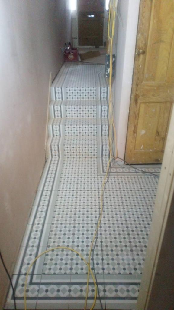 Ułożona podłoga i schody w biało-szarą mozaikę z ciemnymi punktami, widoczne kable elektryczne i narzędzia w tle.