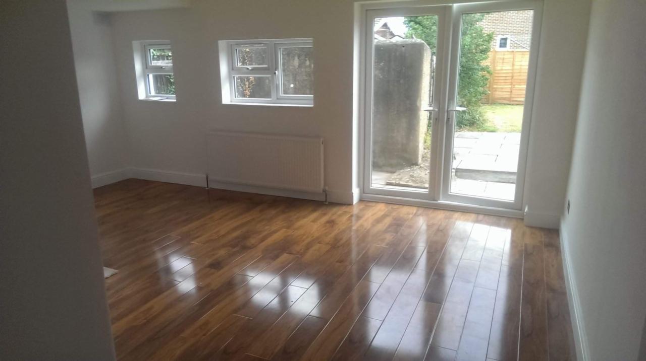 Puste pomieszczenie z nową, błyszczącą podłogą z paneli drewnopodobnych, świeżo pomalowanymi na biało ścianami, nowymi oknami PCV i białym grzejnikiem.