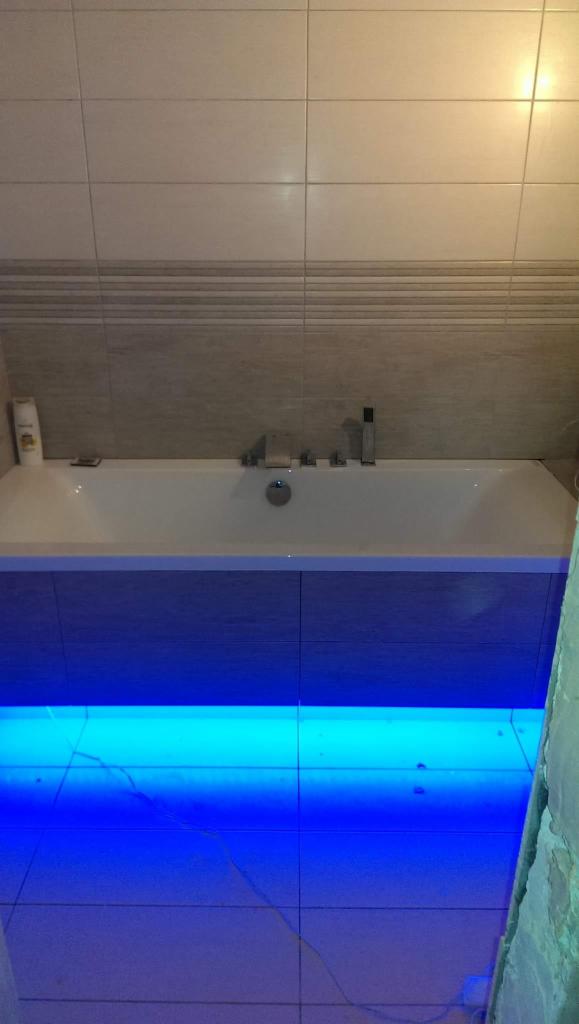 Wykończona łazienka z podświetlaną wanną, beżowe płytki na ścianie i podłodze, widoczny fragment ściany w trakcie prac wykończeniowych.