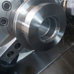 Metalowy element z gwintem wewnętrznym, zamocowany w uchwycie tokarskim podczas obróbki. Widoczne ślady chłodziwa i wióry.