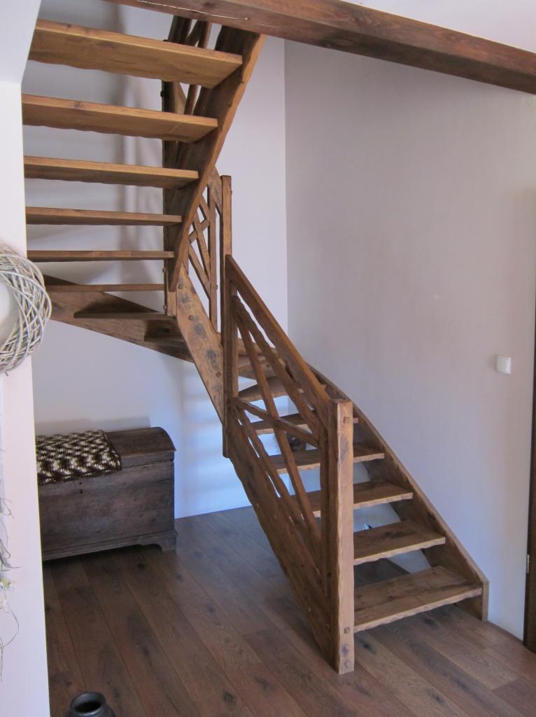 Drewniane schody z balustradą o kratownicowej konstrukcji w domu w Trzemesznie, widoczne od dołu, obok skrzynia z wzorzystym pledem.