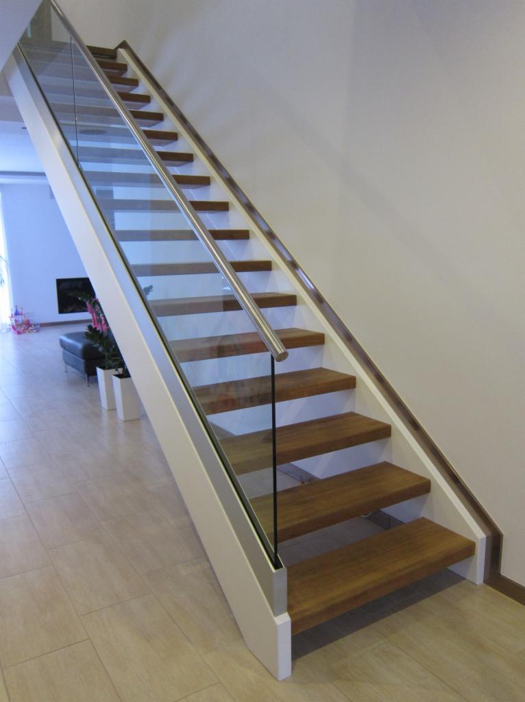 Nowoczesne schody z drewnianymi stopniami, białą konstrukcją i szklaną balustradą z metalową poręczą, widok z dołu.