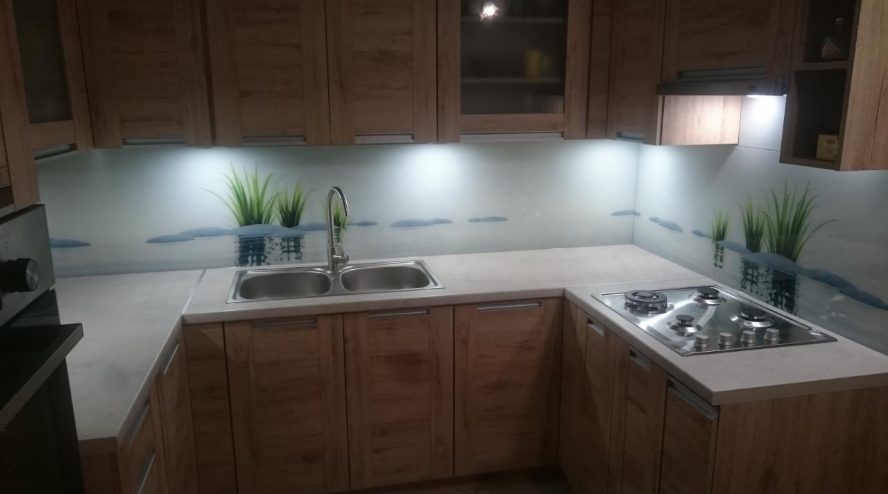 Szklany panel ścienny w kuchni z motywem jeziora i trawy, podświetlony od góry, z widocznym zlewem dwukomorowym i płytą gazową.