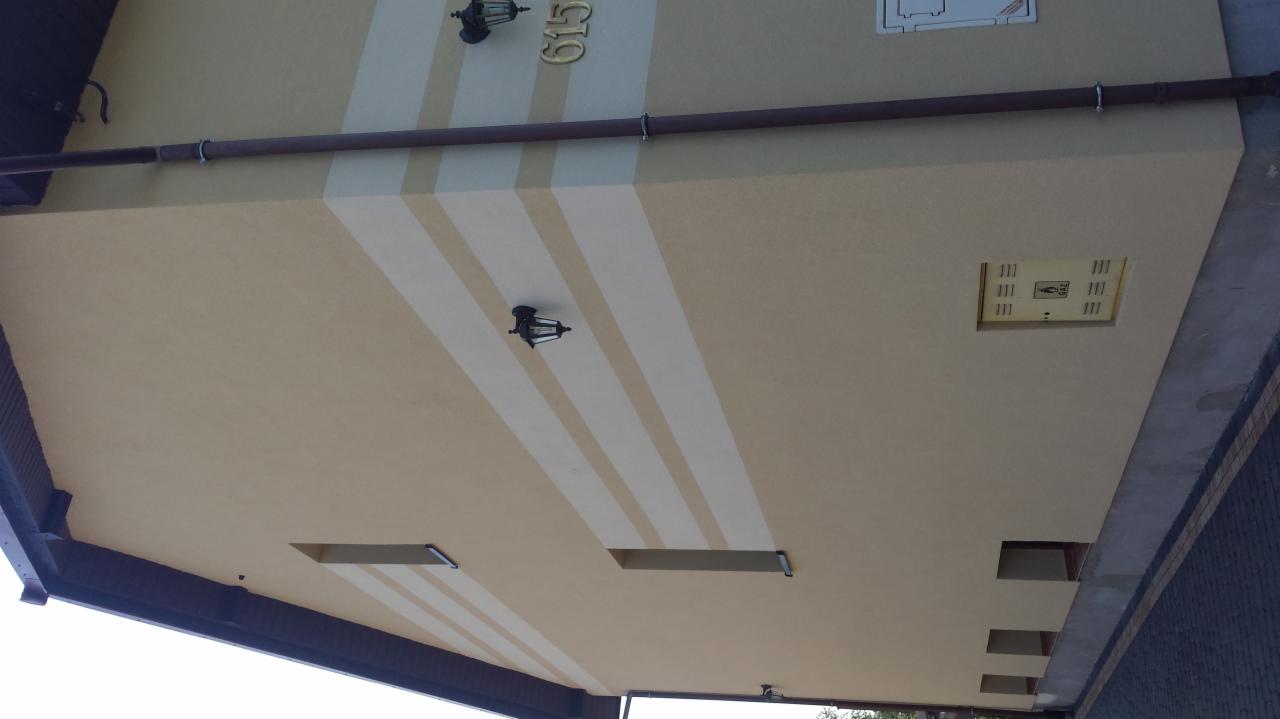 Elewacja budynku z beżowym tynkiem i białymi pasami, oświetlona lampami w stylu retro, z widocznym numerem domu 615 oraz skrzynką wentylacyjną.