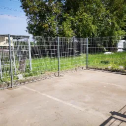 Nowoczesne, metalowe ogrodzenie panelowe na betonowej powierzchni w Cieszkowie, z widoczną zielenią w tle i elementami do suszenia prania.