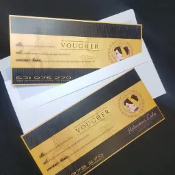 Dwa eleganckie vouchery rabatowe w kolorach czerni i złota, z logo firmy Malowana Lala Ewa Kotwica, leżące na białej kopercie na ciemnym tle.