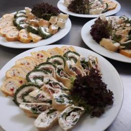 Pierogowa Panna - Trzy białe talerze z roladkami mięsnymi i warzywnymi, udekorowane ciemną sałatą na metalowym blacie.