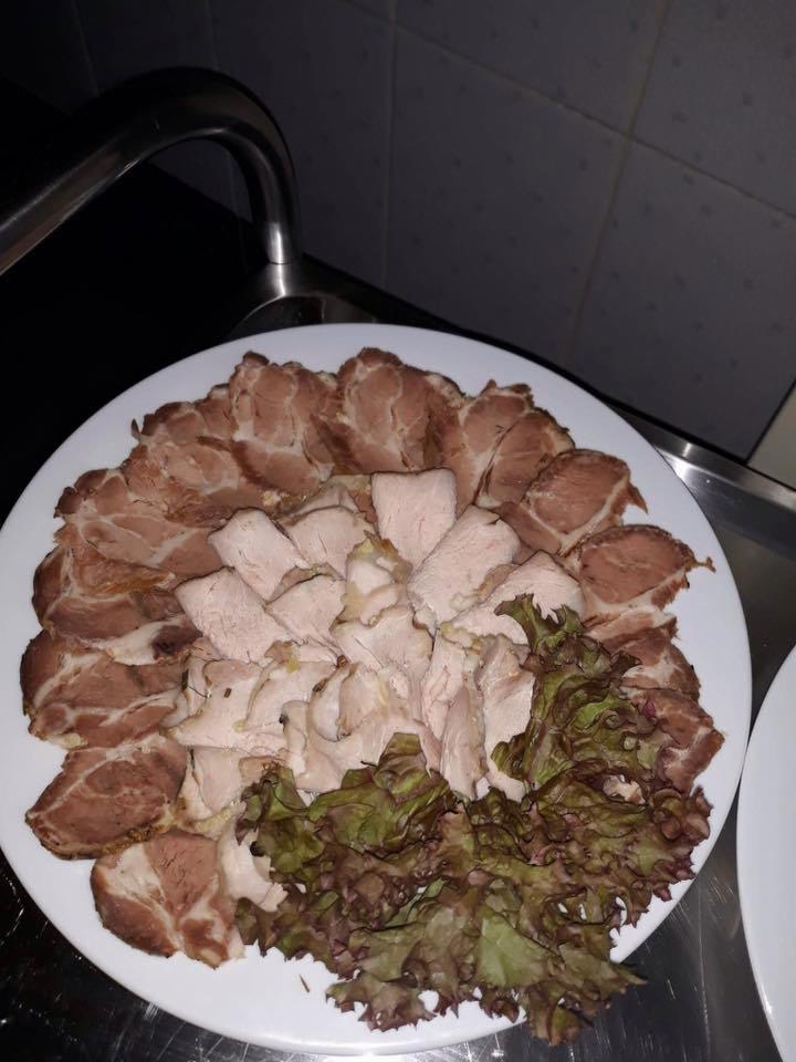 Talerz z plastrami pieczonego mięsa i sałatą na metalowym blacie, widoczny kran i płytki w tle.