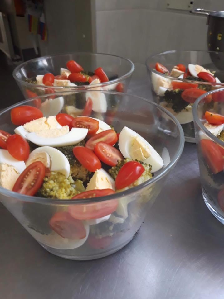 Szklane miseczki z sałatką: brokuły, pomidorki koktajlowe, jajko na twardo i ser feta, ustawione na metalowym blacie, przygotowane do serwowania.