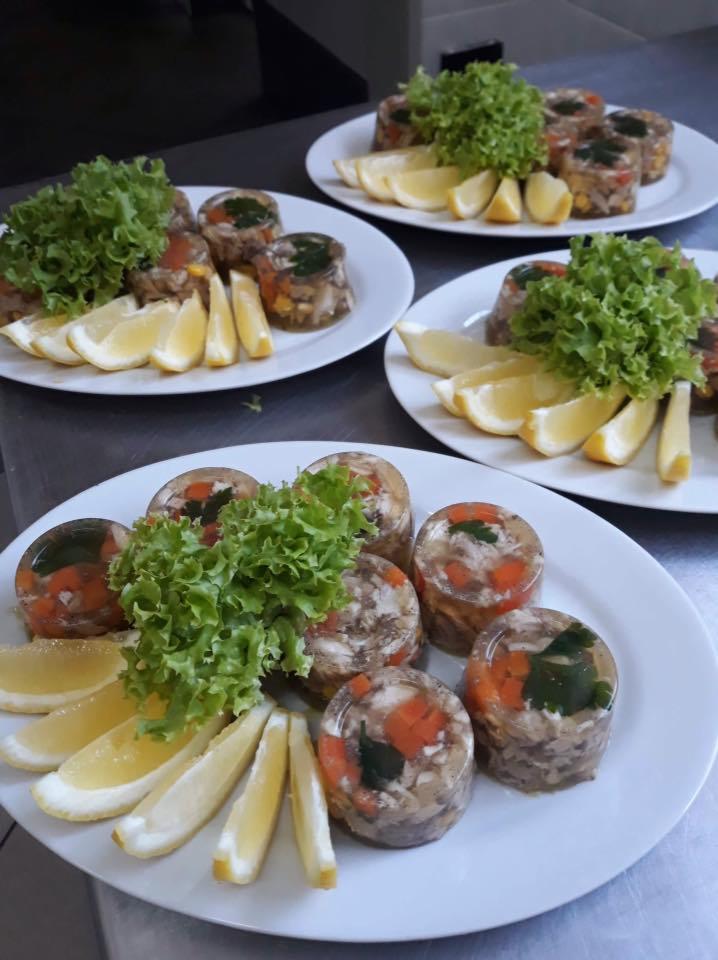 Trzy białe talerze z galaretką wieprzową z warzywami, udekorowaną sałatą i ćwiartkami cytryny, gotowe do serwowania.