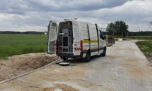 Samochód serwisowy z otwartymi tylnymi drzwiami na betonowej drodze w Srocku, z widocznym sprzętem hydraulicznym wewnątrz, sugerujący prace instalacyjne na zewnątrz budynków.