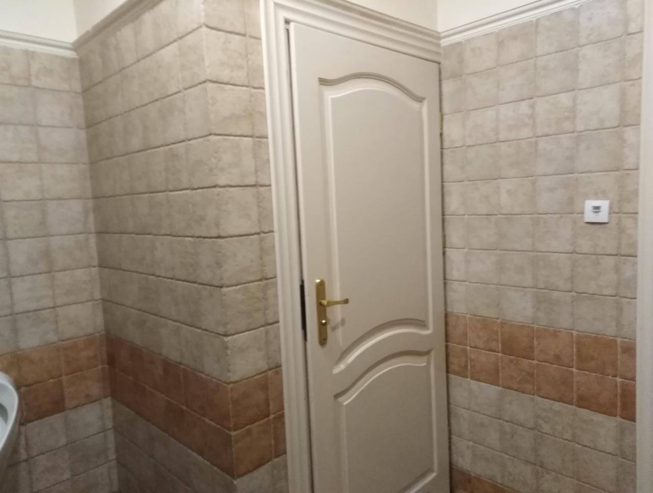Wykończona łazienka z beżowymi i brązowymi płytkami imitującymi cegłę, białe drzwi z ozdobnym frezem i złotą klamką oraz włącznik światła na ścianie.