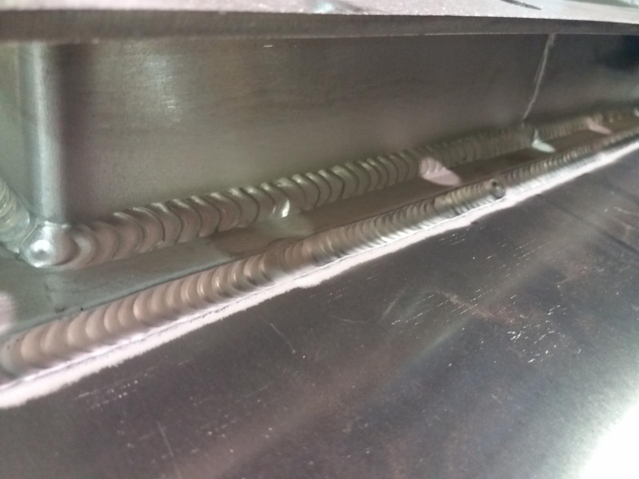 Szczegółowe zbliżenie spawu TIG na metalowej konstrukcji, widoczne precyzyjne spoiny z charakterystycznymi łuskami, minimalne przypalenia i refleksy świetlne na powierzchni metalu.