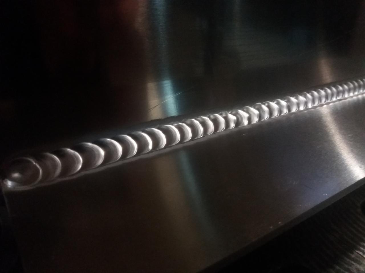 Precyzyjny spaw na gładkiej, metalowej powierzchni, widoczny w zbliżeniu, z delikatnym odblaskiem światła.