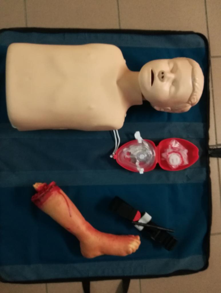 Manekin do ćwiczeń resuscytacji z otwartą maską i atrapa zranionej nogi z opaską uciskową na niebieskiej macie