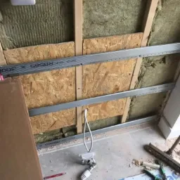 Montaż izolacji z wełny mineralnej i konstrukcji metalowej pod okładzinę sufitową, widoczne narzędzia i przewód elektryczny.