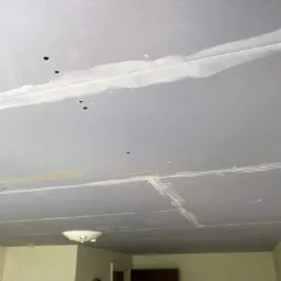 Szpachlowana powierzchnia sufitu z widocznymi łączeniami płyt i punktowymi otworami, przygotowana do dalszego wykończenia, z zamontowaną lampą sufitową.