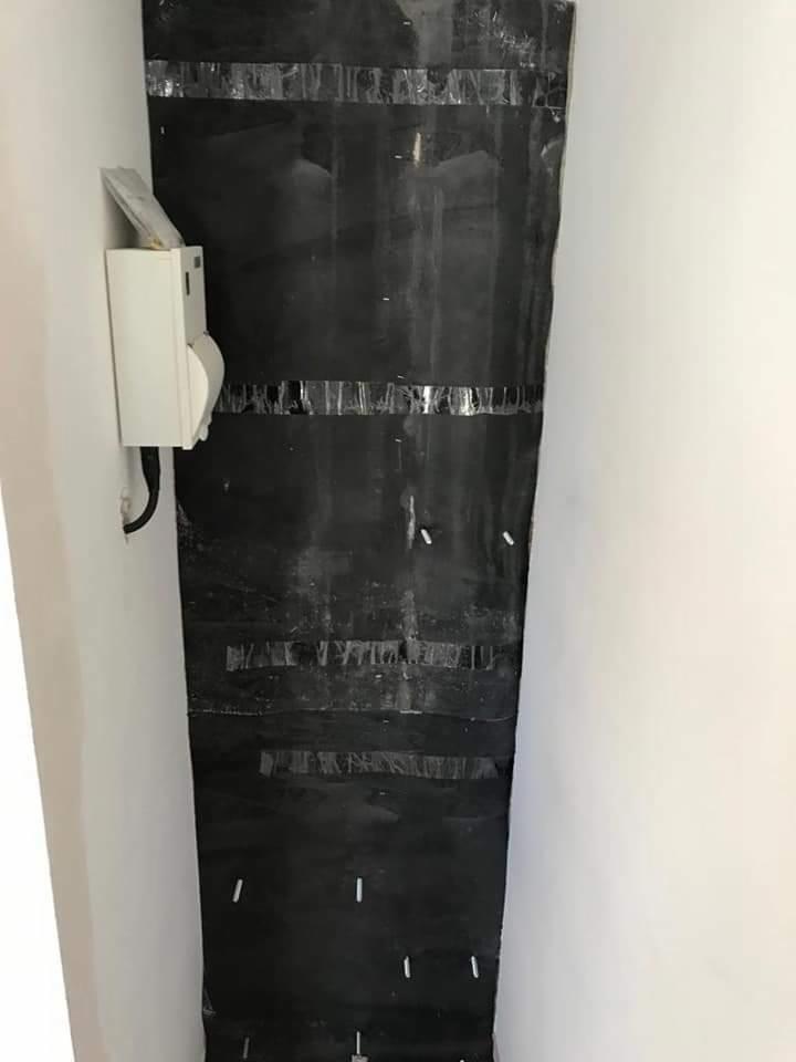 Czarne zabezpieczenie z folii przymocowane do ściany taśmą, prawdopodobnie podczas prac remontowych, widoczny biały przełącznik na ścianie obok.